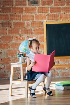 Cute little girl in school uniform posing next to school board with book in her hands, back to school concept