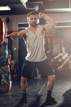 Young muscular man doing hard exercise with dumbbell on cross training at the gym.