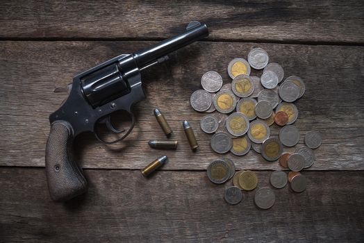 Gun and coins on wooden table. top view