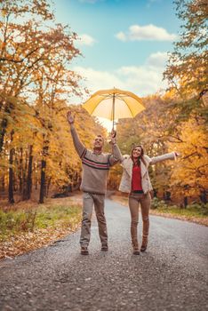 Beautiful cheerful young couple with yelow umbrella having fun in sunny park in autumn colors.