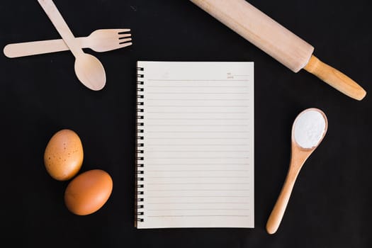 Baking cake ingredients,recipe book,spoon, flour, eggs, egg beater, rolling pin and eggshells on dark table