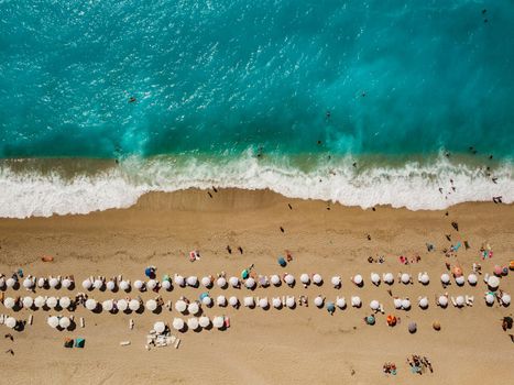 Aerial view of the amazing  idyllic  beach with white umbrellas, sunbed and people who sunbathing and swiming.