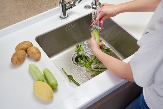 Cropped view of female hands peeling cucumber over Food waste disposer machine 