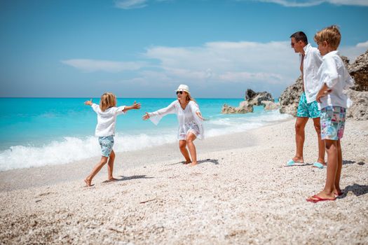 Beautiful little boy enjoying with his mother on the beach. He is running along the beach into his mother's hug. His father and brother are looking at them.