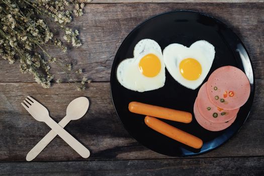 Fried egg on heart-shaped with ham and sausage on wood table