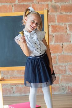 Portrait of caucasian school kindergarten girl standing in front of blackboard with a bell in her hands, back to school concept