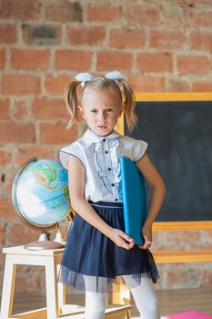 Unhappy little girl in school uniform with a book in her hands, back to school concept