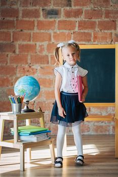 Cute little girl in school uniform posing next to school board with book in her hands, back to school concept