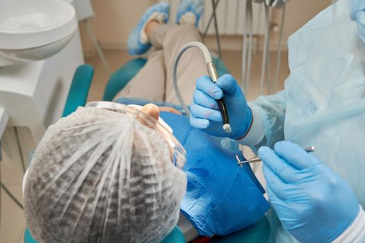 Lady patient sitting in stomatology chair, dentist drilling tooth, modern clinic
