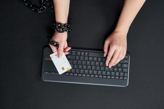 Woman with metal chain holding credit card over keyboard, online buying addiction concept