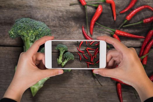 mobile take photo over fresh broccoli and chilli on wood table background. top view