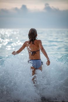 A little girl having fun in the waves of the sea and the drops of water are splashing all over her.
