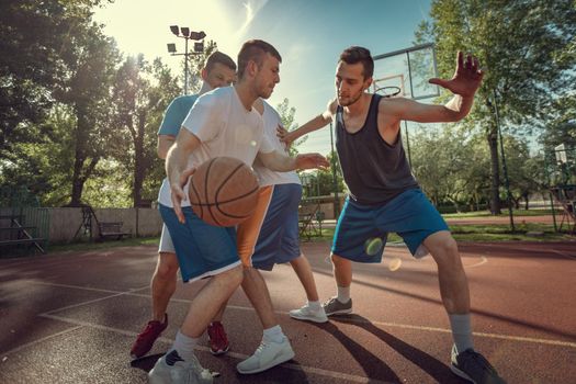 Four basketball players have a training outdoor. They are playing and making action together.