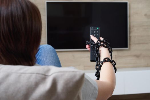 TV addiction and dependency concept. Female hand tied to the remote with the chain