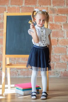 Cute little girl in school uniform posing next to school board with a bell in her hands, back to school concept