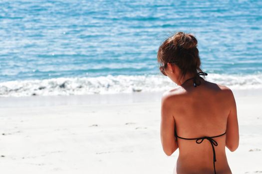 Woman wearing black bikini on a sunny beach.