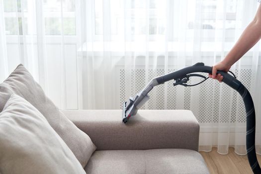 Young housewife Cleaning the Sofa with Vacuum Cleaner in living room