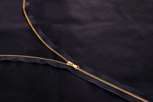 Open golden zipper on black fabric
