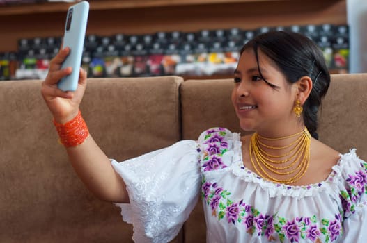 beautiful indigenous woman in traditional dress from otavalo ecuador smiling while taking a selfie with her cell phone. High quality photo