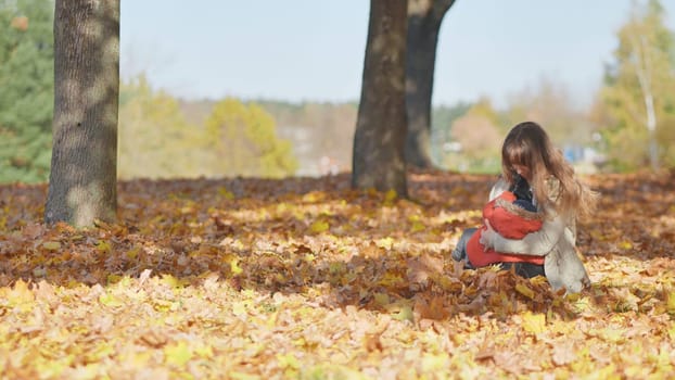 A mother and child in the park in the fall sitting on fallen leaves