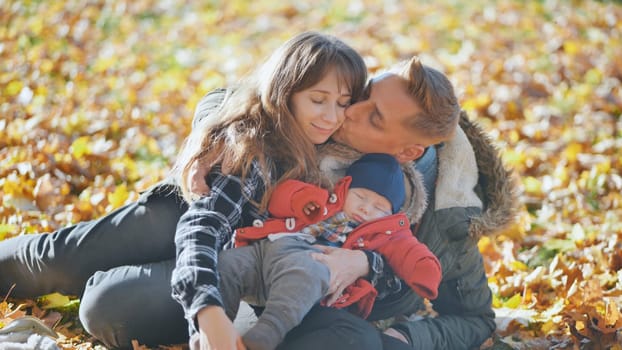 A family and their children enjoy the golden fall in the park sitting on the leaves
