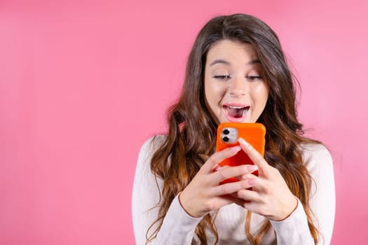 Portrait of young woman emotionally looking at the phone after winning the lottery on the pink background
