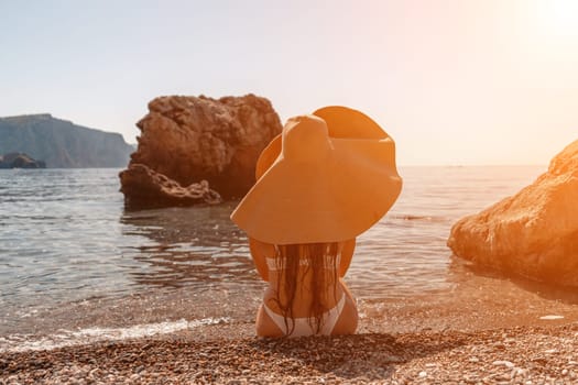 woman sea travel Tanned middle-aged woman with long hair and a white bathing suit. He sits on the seashore in a large sun hat with his back and looks at the sea