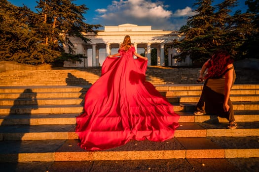 Sunrise red dress. A woman in a long red dress against the backdrop of sunrise, bright golden light of the sun's rays. The concept of femininity, harmony