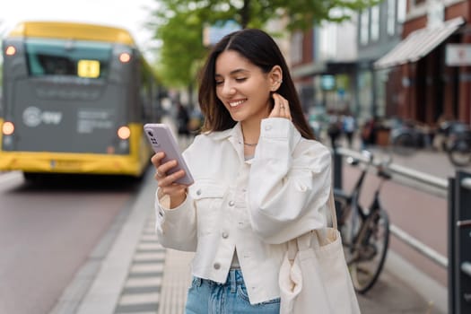 Happy commute on public transport. Multi-ethnic attractive woman with beautiful smile at bus station looking at phone.