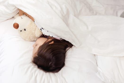 Cute little child girl sleeping with teddy bearin her bed. top view