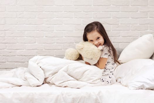 adorable little child girl hugging teddy bear in bed in morning.