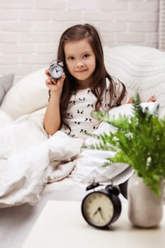 cute happy little child girl in pyjamas with clock in bed. good morning