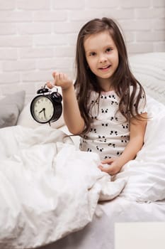 cute happy little child girl in pyjamas with clock in bed. good morning