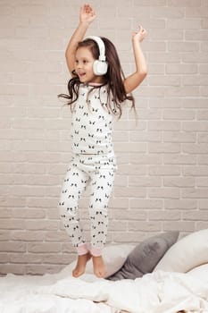 little child girl listening to the music with the headphones and dancing on bed. happy morning