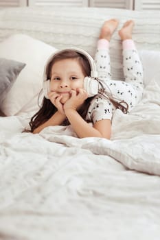 little child girl listening to the music with the headphones on bed. happy morning
