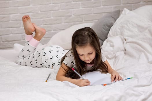 cute little girl drawing pictures while lying on bed. Kid painting at home