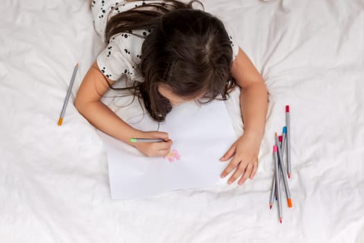 cute little girl drawing pictures while lying on bed. Kid painting at home
