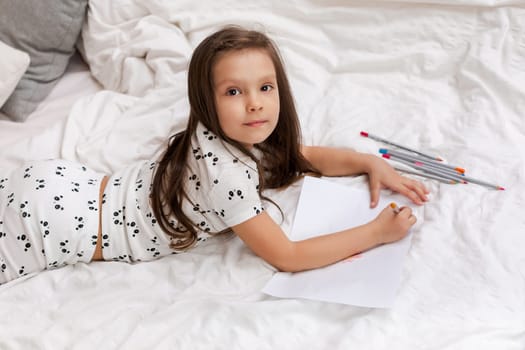 cute little girl drawing pictures while lying on bed. Kid painting at home