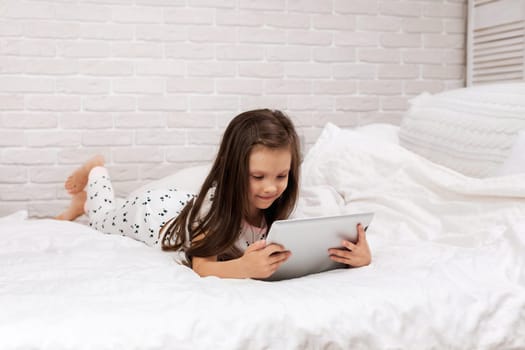 cute little child girl lies in bed uses digital tablet. child playing on tablet pc.