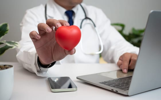 A Doctor holding and showing a red heart at hospital office. Medical health care and doctor staff service concept. 
