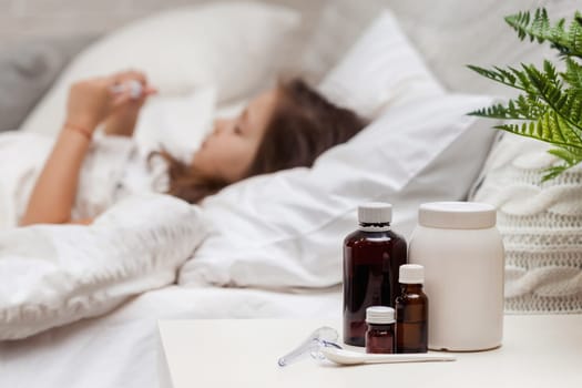 Sick little child girl lying in bed with thermometer. Cold flu season. focus on medication
