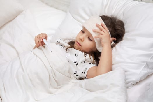 Sick little child girl lying in bed with thermometer. Cold flu season