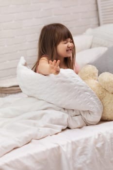 cute little child girl wakes up from sleep in bed. child shows gesture stop. I do not want to get up