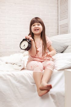 smiling little child girl in pyjamas with clock in bed. good morning