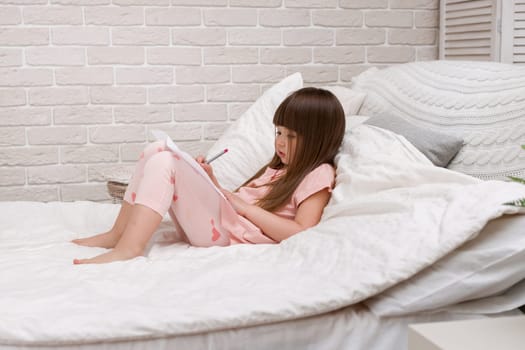 cute little girl drawing pictures while lying on bed. Kid painting at home