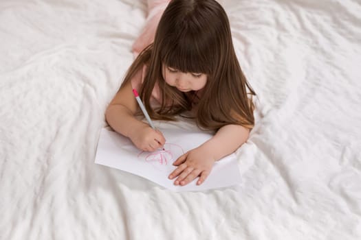 cute little girl drawing pictures while lying on bed. Kid painting at home. top view