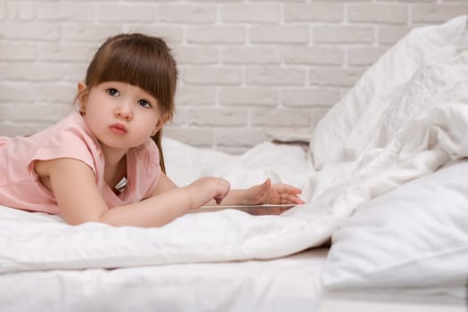cute little child girl lies in bed uses digital tablet. child playing on tablet pc. space for text
