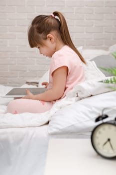 cute little child girl lies in bed uses digital tablet. child playing on tablet pc.