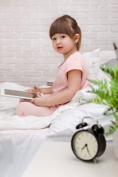 cute little child girl lies in bed uses digital tablet. child playing on tablet pc.