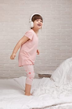 little child girl listening to the music with the headphones and dancing on bed. happy morning